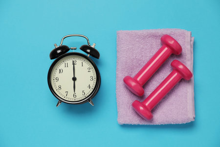 Alarm clock, towel and dumbbells on light blue background, flat lay. morning exerciseの写真素材