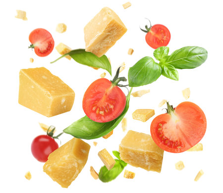 Pieces of delicious parmesan, tomatoes and basil leaves falling on white backgroundの写真素材