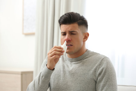 Ill man using nasal spray at home