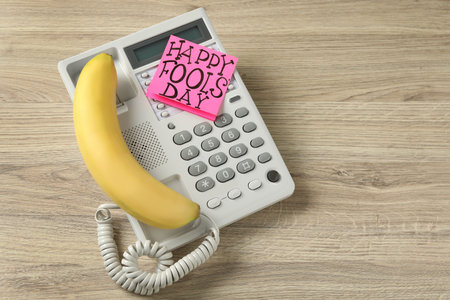 Corded phone with banana as handset and words Happy Fool's Day on wooden table, above view. Space for textの写真素材