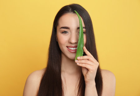 Young woman with aloe vera leaf on yellow backgroundの写真素材