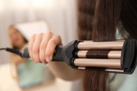 Young woman using modern curling iron indoors, closeupの写真素材