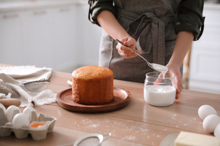 Young woman decorating traditional Easter cake with glaze in kitchen, closeupの写真素材