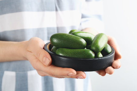 Woman holding black wooden bowl with fresh seedless avocados, closeupの写真素材