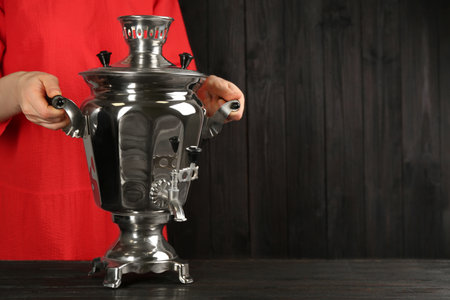 Woman holding traditional Russian samovar on dark wooden background, closeup. Space for textの写真素材