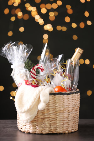 Wicker basket with Christmas gift set on gray table against festive lightsの写真素材