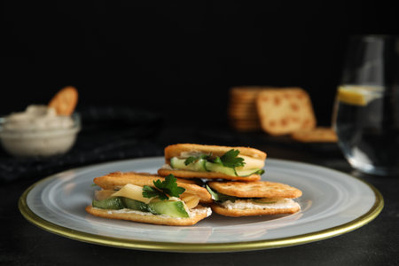 Delicious crackers with cream cheese, cucumber and parsley on black table, closeupの写真素材