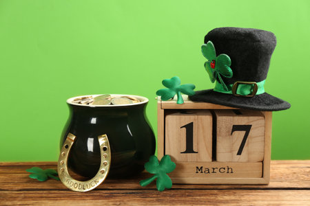 Composition with leprechaun hat, block calendar and pot of gold on wooden table against green...