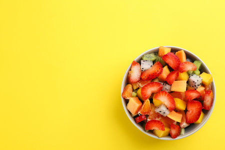Delicious exotic fruit salad on yellow background, top view. Space for textの写真素材