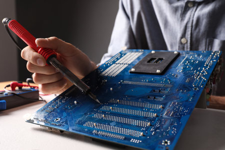 Technician repairing electronic circuit board with soldering iron at table, closeupの写真素材