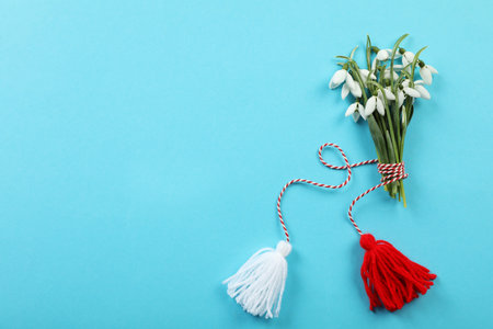 Beautiful snowdrops with traditional martisor on light blue background, flat lay and space for text. Symbol of first spring dayの写真素材