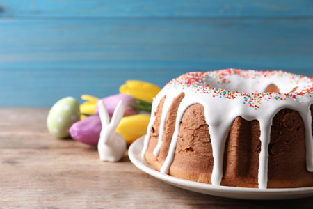 Glazed Easter cake with sprinkles, decorative bunny, painted egg and tulips on wooden table,...