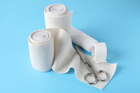 Medical bandage rolls, sticking plaster and scissors on light blue backgroundの写真素材