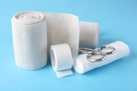 Medical bandage rolls, sticking plaster and scissors on light blue backgroundの写真素材