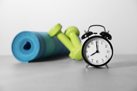 Alarm clock, yoga mat and dumbbells on gray background. morning exerciseの写真素材