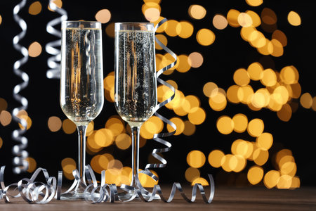 Glasses of champagne and serpentine streamers against black background with blurred lights. Space for textの写真素材