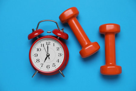 Alarm clock and dumbbells on light blue background, flat lay. morning exerciseの写真素材