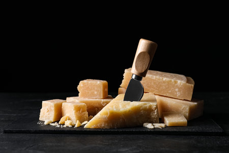 Parmesan cheese with slate plate and knife on black tableの写真素材