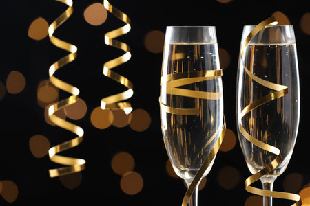 Glasses of champagne and serpentine streamers against black background with blurred lights, closeup. Space for textの写真素材