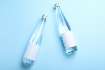 Glass bottles of water with blank label on light blue background, flat layの写真素材