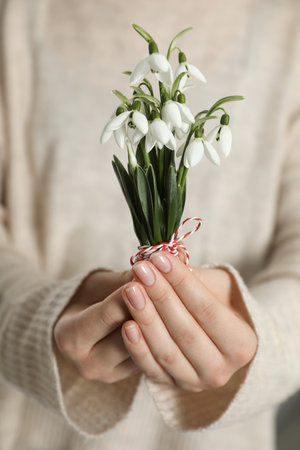 Woman holding beautiful snowdrops with traditional martisor, closeup. Symbol of first spring dayの写真素材