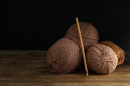 Soft woolen yarns and knitting needle on wooden table against dark background, space for textの写真素材