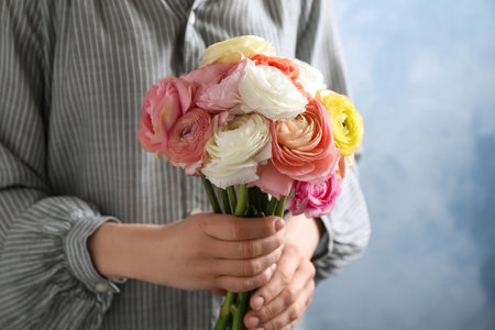 Woman holding beautiful ranunculus flowers against light blue background, closeup