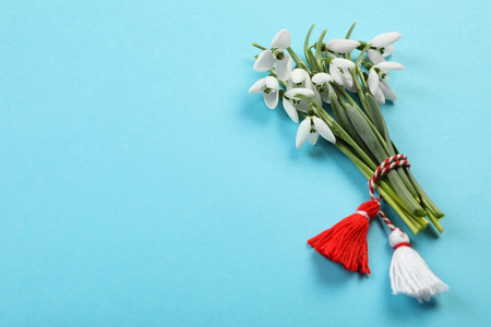 Beautiful snowdrops with traditional martisor on light blue background, flat lay and space for text. Symbol of first spring dayの写真素材