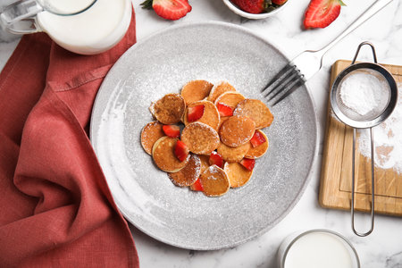 Delicious mini pancakes cereal with strawberries served on white marble table, flat layの写真素材
