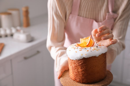 Young woman with traditional decorated Easter cake in kitchen, closeup. Space for textの写真素材