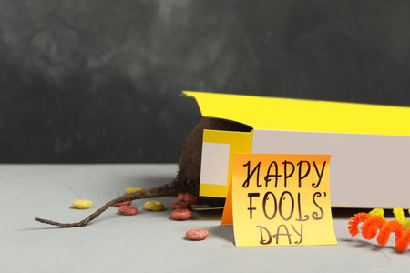 Words Happy Fool's Day and box of corn rings with fake rat's tail on light gray table. Space for textの写真素材