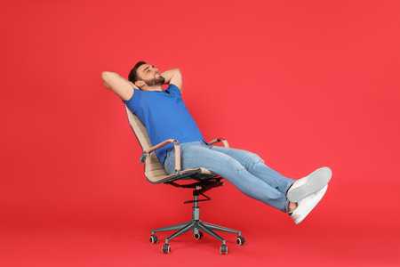 Young man relaxing in comfortable office chair on red backgroundの写真素材