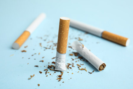 Broken and whole cigarettes on light blue background, closeup. Quitting smoking conceptの写真素材
