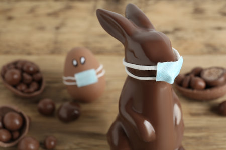 Chocolate bunny in protective mask on table, space for text. Easter holiday during COVID-19 quarantineの写真素材