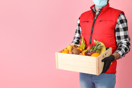 Courier holding crate with assortment of exotic fruits on pink background, closeup. Space for textの写真素材