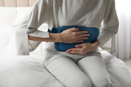 Woman using hot water bottle to relieve abdominal pain on bed at home, closeupの写真素材