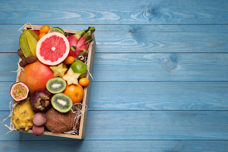 Different tropical fruits in box on blue wooden background, top view. Space for textの写真素材