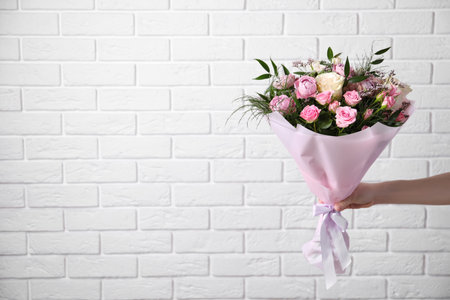Woman with bouquet of beautiful roses near white brick wall, closeup. Space for textの写真素材