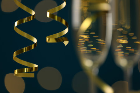 Shiny serpentine streamers and glasses of champagne on dark blue background with blurred lights, closeupの写真素材