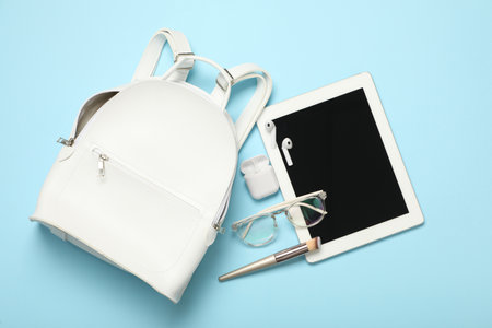 Stylish urban backpack with different items on light blue background, flat lay