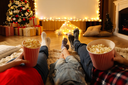 Family with popcorn watching movie on projection screen in room decorated for Christmas, closeup. Home TV equipmentの写真素材