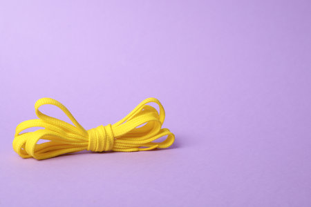 Yellow shoe lace tied in bow on lilac background. Space for textの写真素材