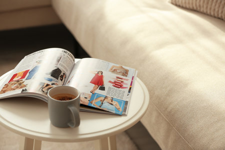 Fashion magazine and cup of hot drink on white table in living roomの写真素材