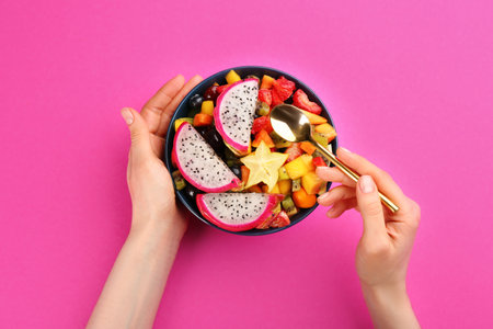 Woman with bowl of delicious exotic fruit salad on pink background, top viewの写真素材