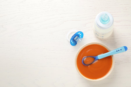 Bowl of healthy baby food, pacifier and bottle with milk on white wooden table, flat lay. Space for textの写真素材