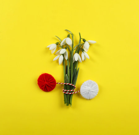 Beautiful snowdrops with traditional martisor on yellow background, flat lay. Symbol of first spring dayの写真素材