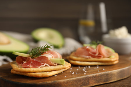 Delicious crackers with avocado, prosciutto and dill on wooden board, closeupの写真素材