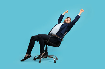 Young businessman stretching in comfortable office chair on turquoise backgroundの写真素材