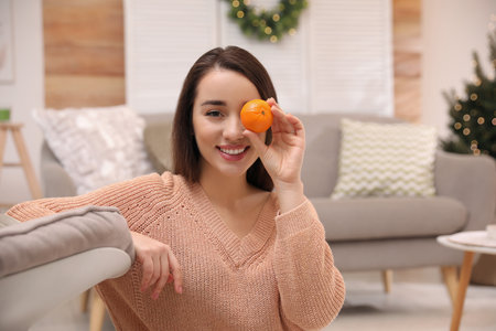 Happy young woman with tangerine in living roomの写真素材