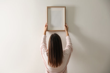 Woman hanging picture on white wall indoorsの写真素材